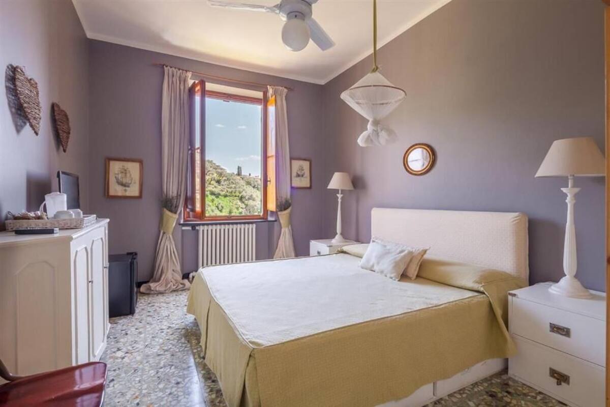 Une chambre à coucher comprenant un lit, des tables de chevet, une fenêtre avec des rideaux, un ventilateur de plafond et des éléments de décoration murale.