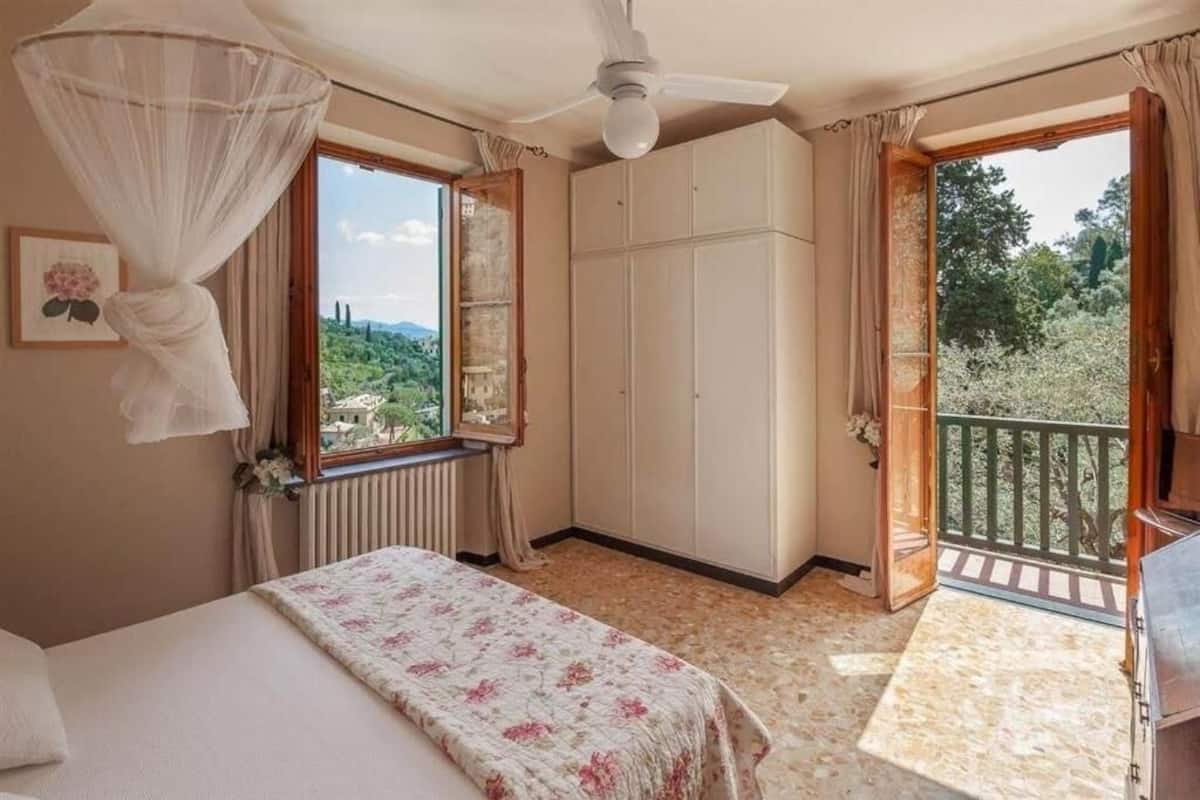 Une chambre à coucher comprenant un lit, un ventilateur de plafond, une fenêtre donnant sur un espace verdoyant et un balcon avec une balustrade.