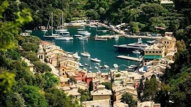 Ein Küstendorf mit einer dichten Bebauung, einer Marina mit Booten und einem markanten Turm auf einem Hügel.
