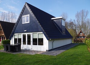 Una casa moderna con techo oscuro, ventanas grandes y un patio con mobiliario exterior.