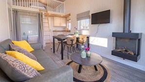 A cozy living room with a sofa, coffee table, and fireplace. A kitchen is visible in the background. - EuroParcs Limburg (Susteren)