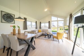 A spacious living room with a dining area, large windows, and a view of the outdoors. - EuroParcs Limburg (Susteren)