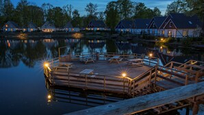 A wooden dock with benches and a railing, extending over calm water with a reflection of nearby buildings. - EuroParcs Limburg (Susteren)