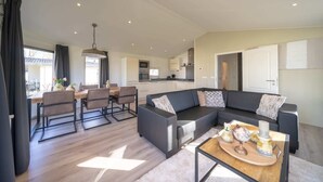 A modern living room with a sectional sofa, a dining area with a table and chairs, and a kitchen in the background. - EuroParcs Limburg (Susteren)