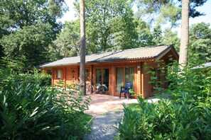 A wooden cabin with a tiled roof, surrounded by lush greenery and trees. - EuroParcs Brunssummerheide (Brunssum)