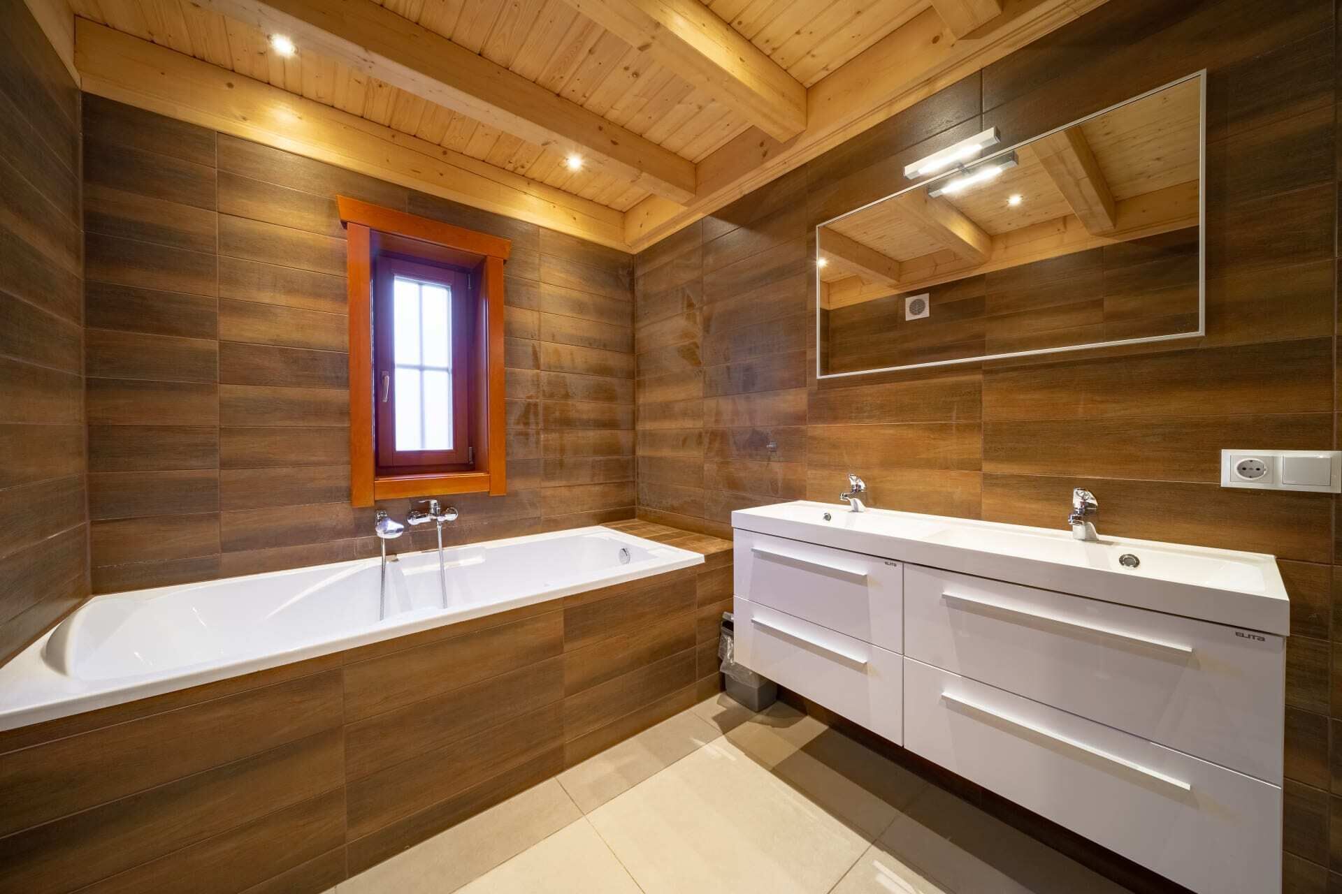 A modern bathroom with a wooden interior, a large bathtub, a double sink vanity, and a mirror above the vanity.