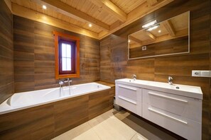Un baño moderno con detalles de madera, una bañera grande, un lavamanos doble y un espejo sobre el lavamanos.