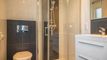 Une salle de bain moderne avec une douche à parois de verre, des toilettes blanches et un meuble-lavabo avec des tiroirs.