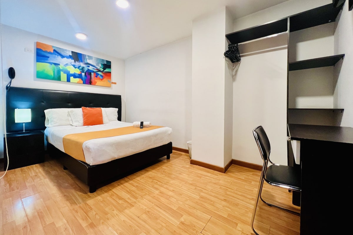 A hotel room with a bed, bedside table, lamp, and a painting on the wall.
