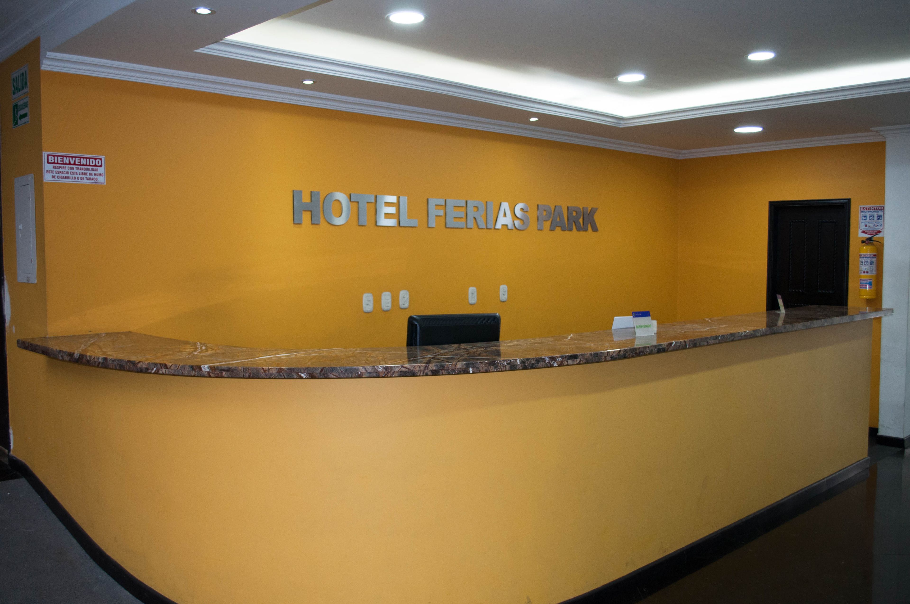 A reception desk with a sign reading "HOTEL FERIAS PARK" and a black door in the background.