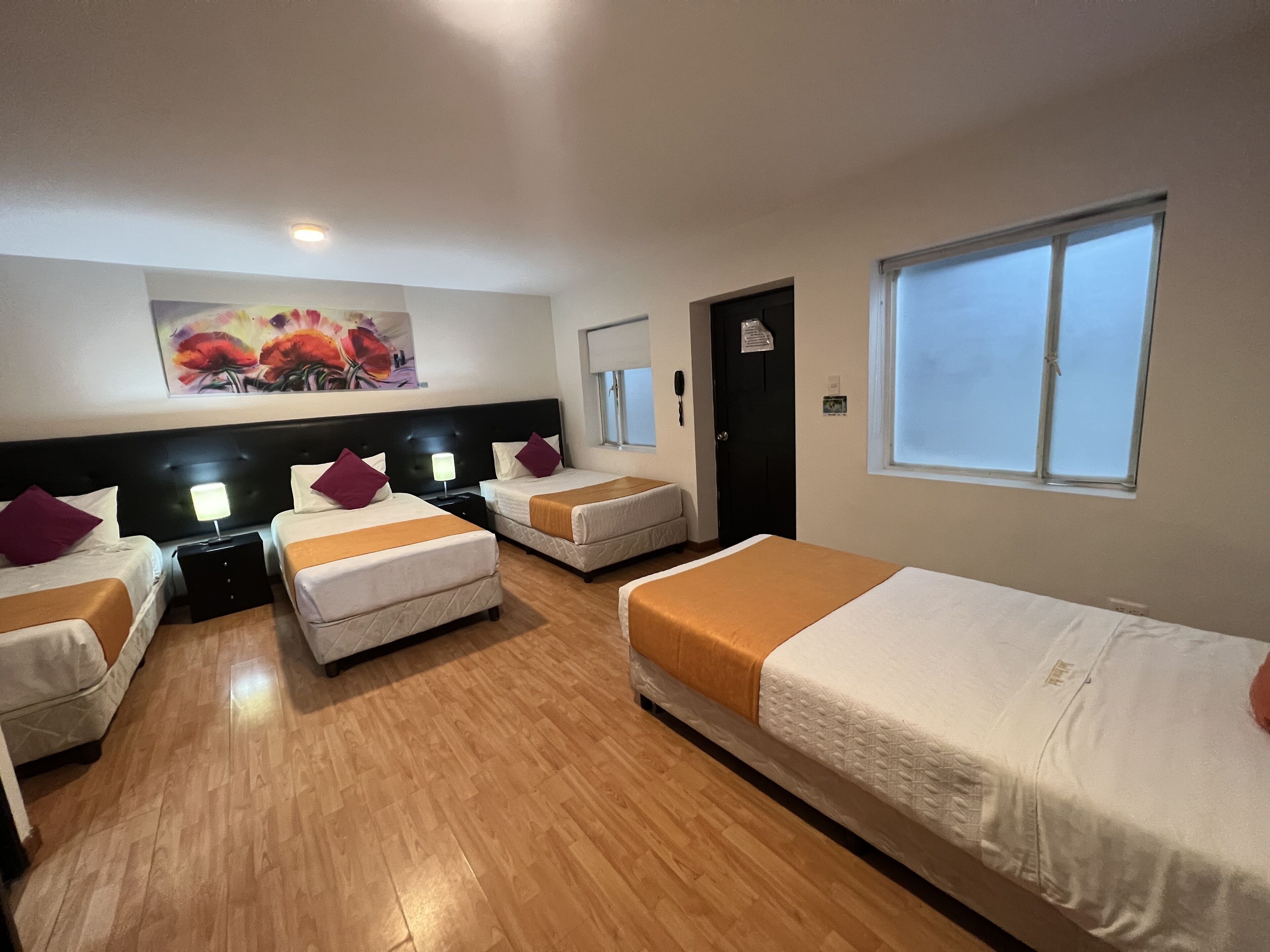 A hotel room with four beds, a painting on the wall, a window, and a door.