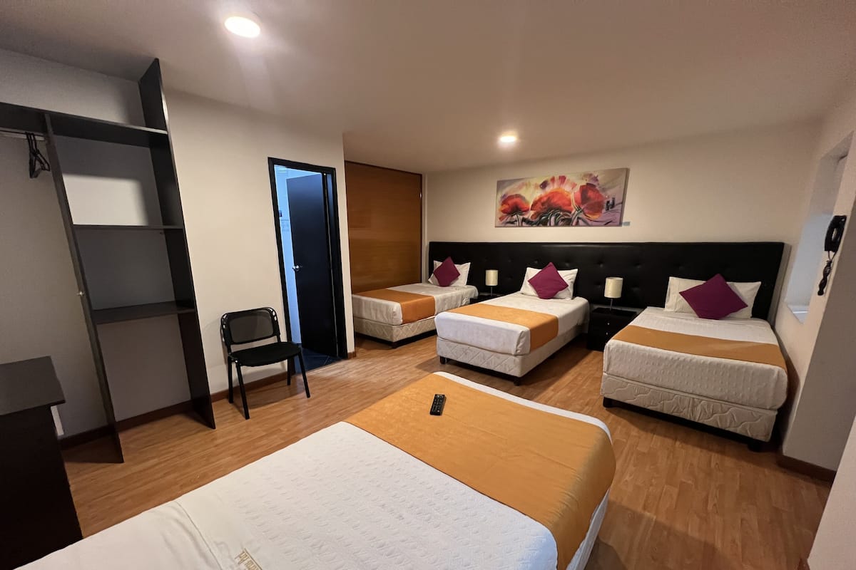 A hotel room with two single beds, a large bed, a chair, a desk, and a bookshelf.