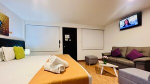Habitación de hotel con cama, sofá, televisión y una mesita.