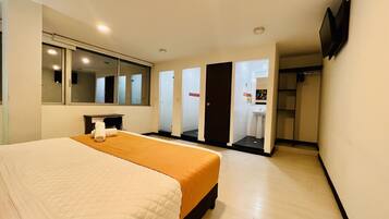 A hotel room with a bed, a desk, a mirror, a TV, and a bathroom visible through an open door.