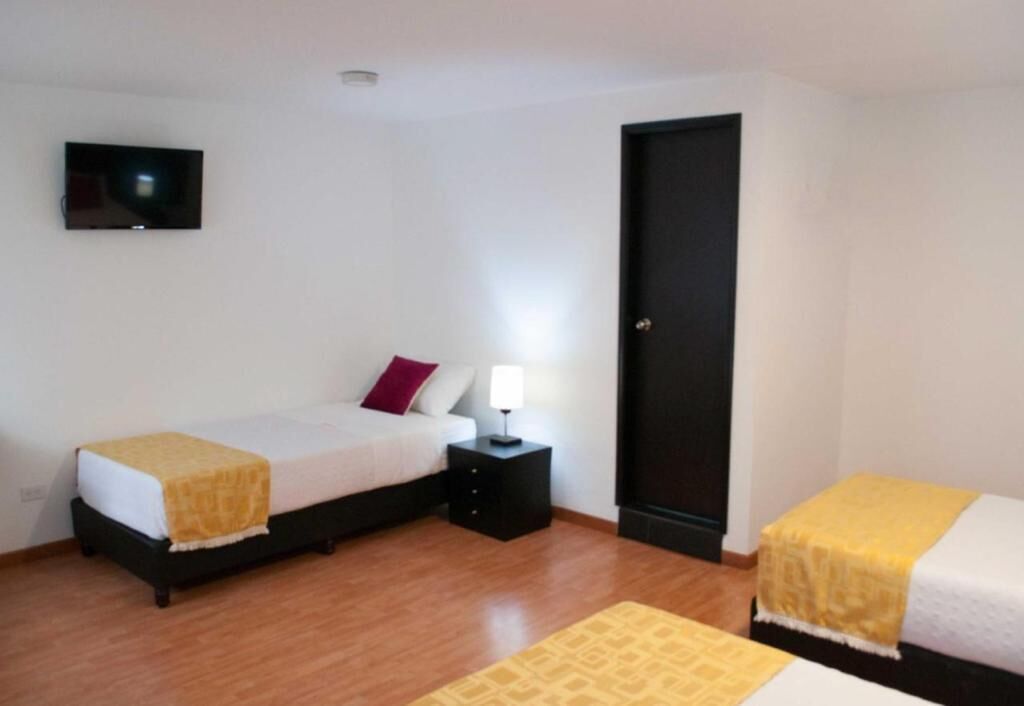 A room with two beds, a TV on the wall, a door, and a nightstand with a lamp.