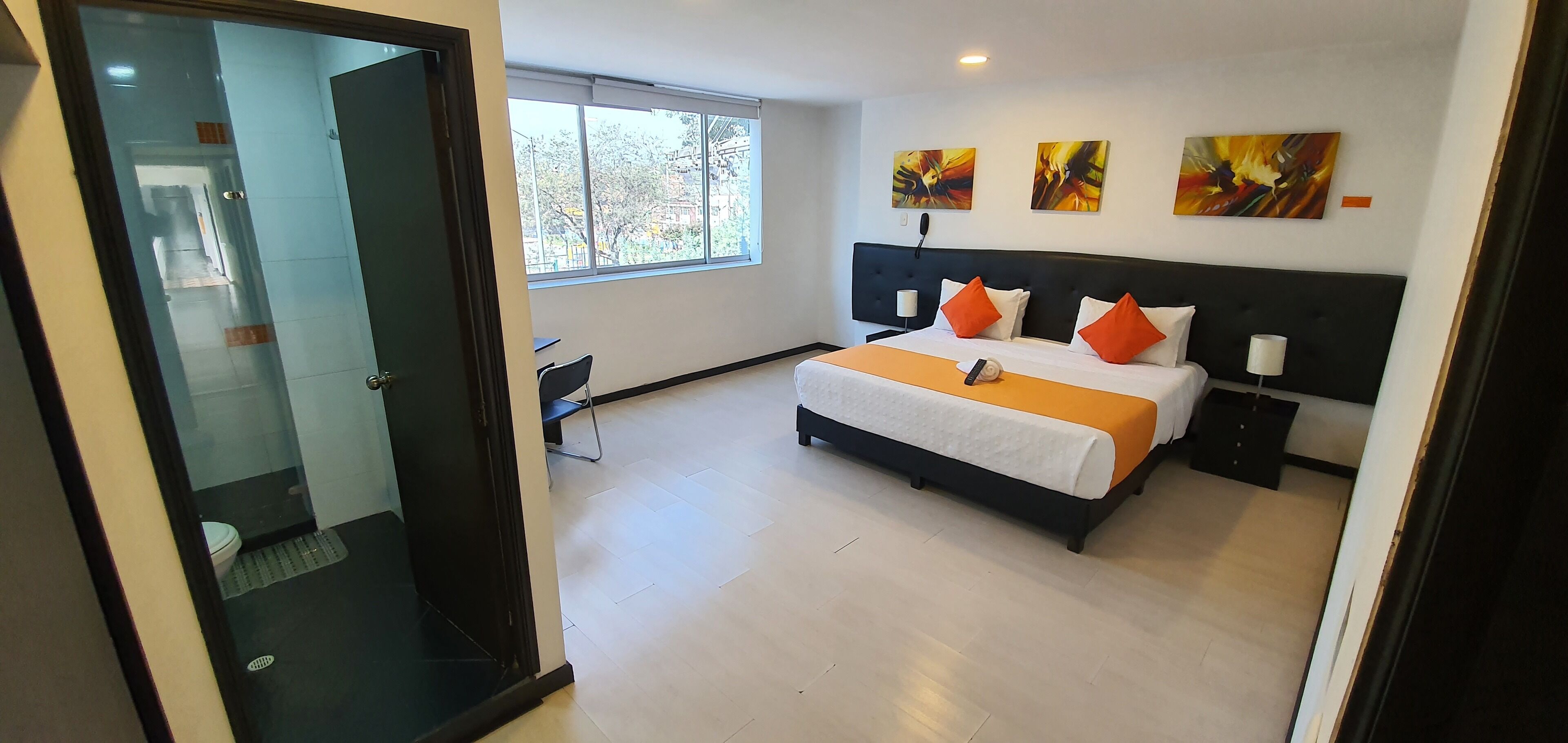 Una habitación de hotel moderna con una cama grande, dos mesitas de noche, un escritorio y un ventanal con vistas a árboles.