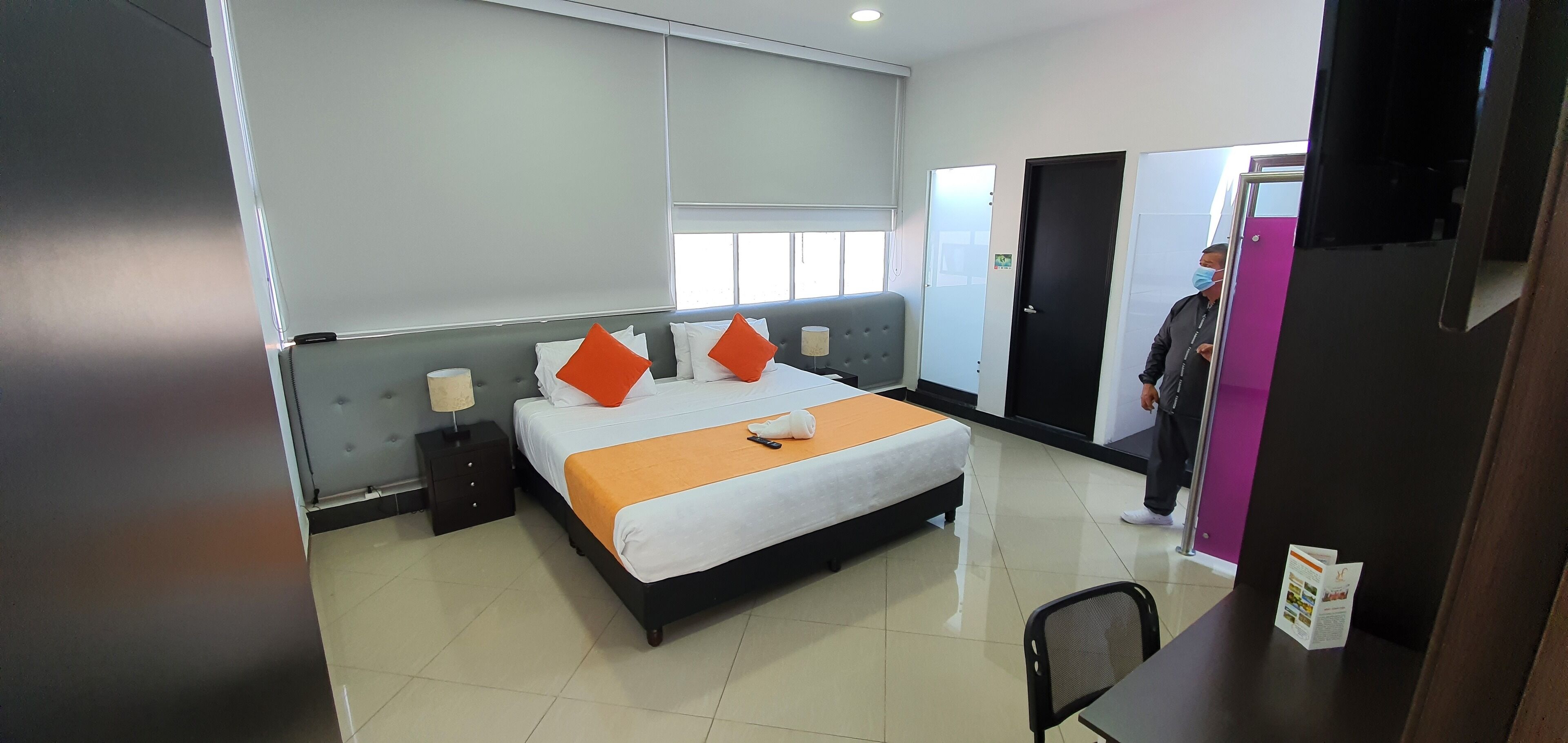 A hotel room with a bed, bedside tables, a window, and a door.