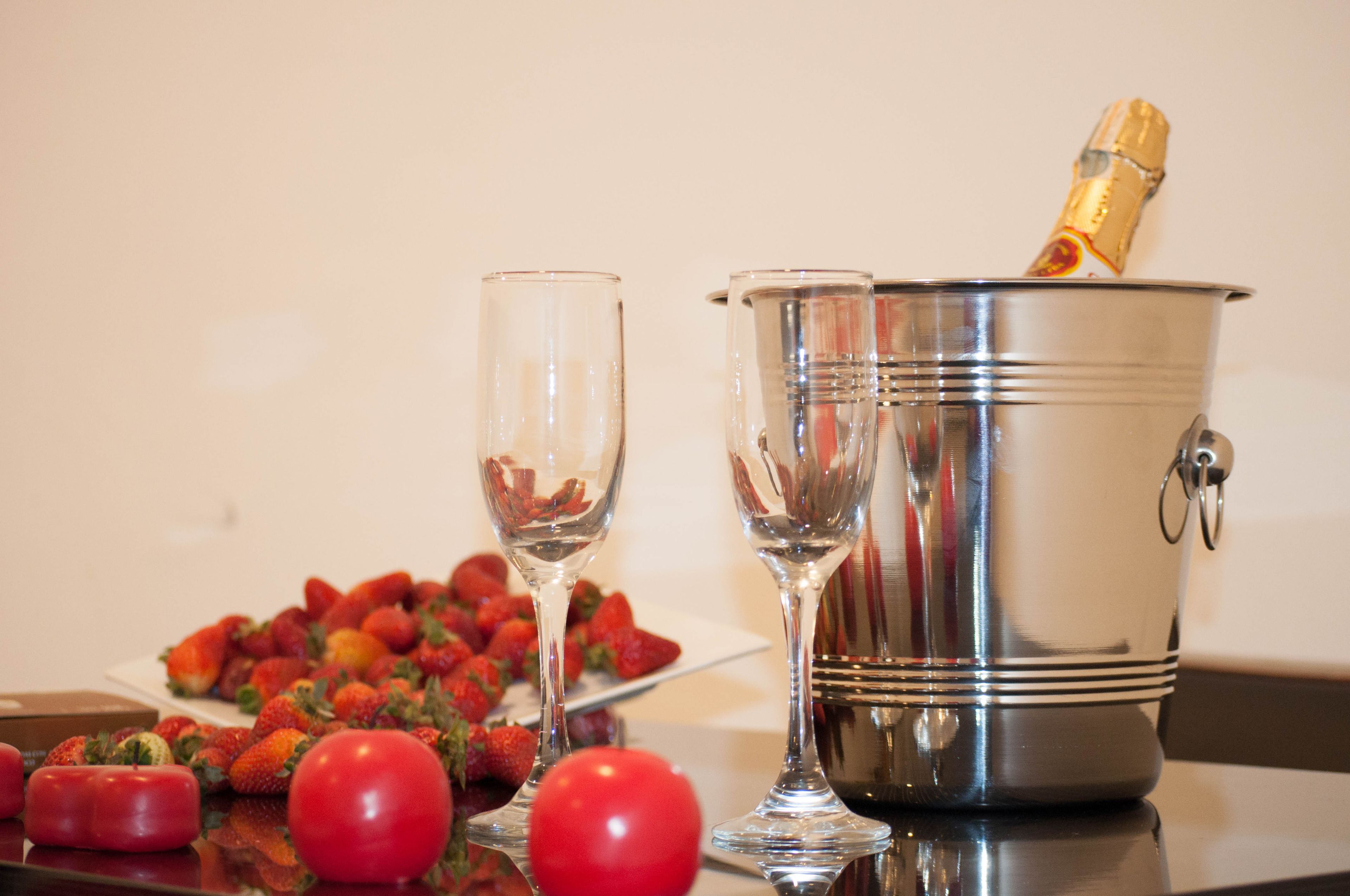 A table with a champagne bottle in a metal bucket, two empty wine glasses, and a plate of strawberries.