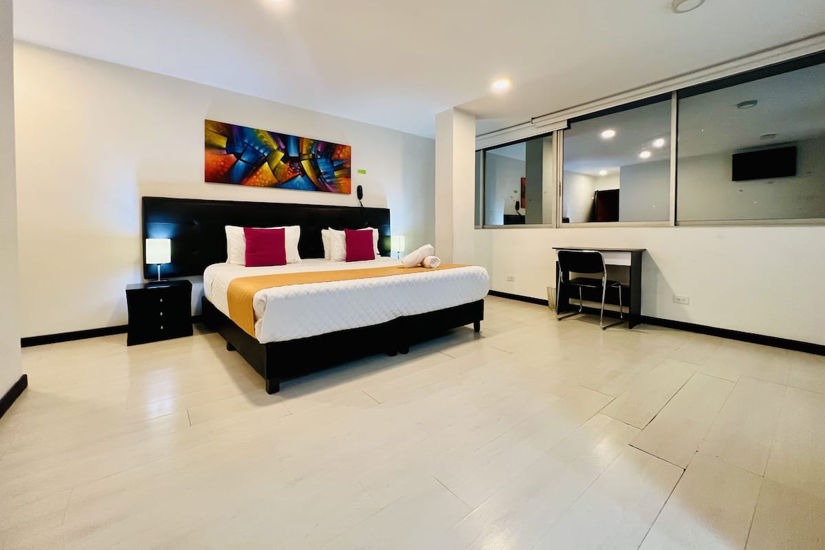 A modern hotel room with a large bed, a desk, and a large window.