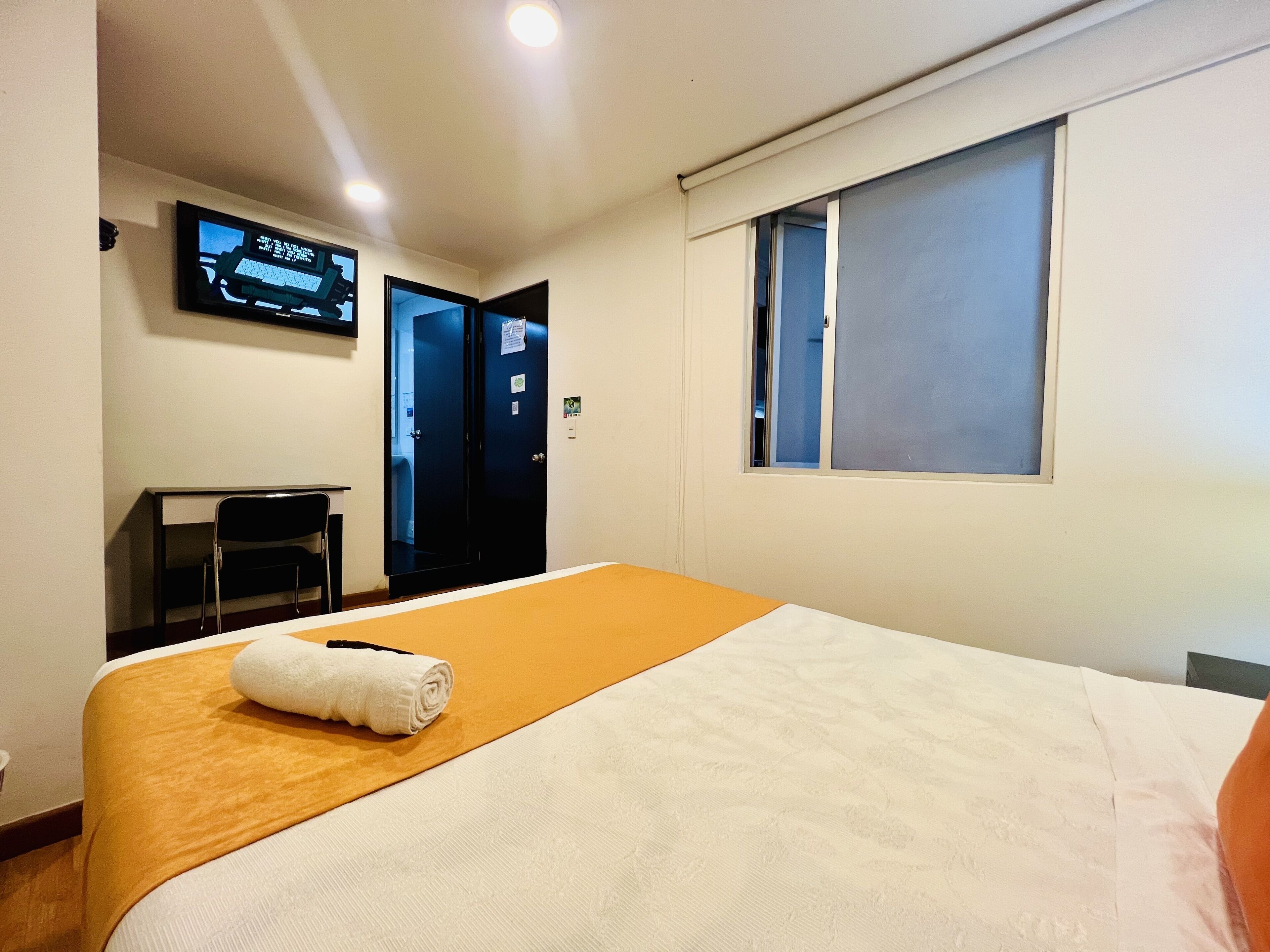 A hotel room with a bed, a TV mounted on the wall, a window, and a door.