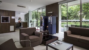 Un vestíbulo moderno con asientos, una máquina expendedora y grandes ventanales que ofrecen vistas a zonas verdes.