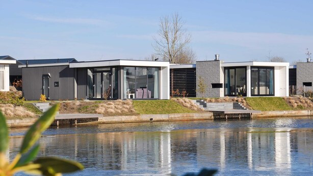 A modern residential building with a glass facade, a small outdoor seating area, and a reflection in the water. - EuroParcs Veluwemeer (Nunspeet)