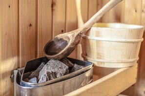 A sauna with a wooden bench, a metal container with charcoal, and a wooden ladle. - EuroParcs Veluwemeer (Nunspeet)