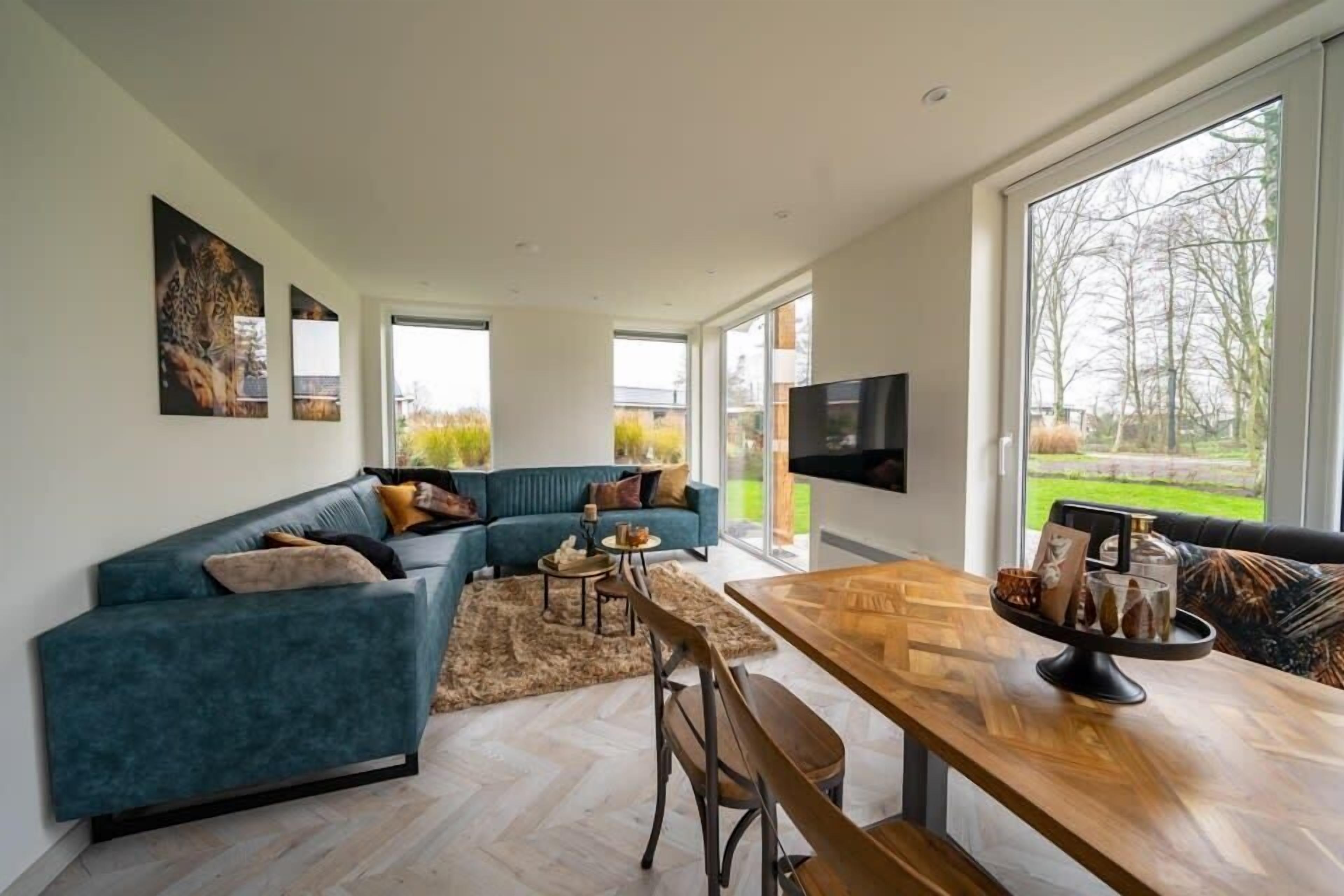 A spacious living area with a large sofa, a wooden dining table, and a TV mounted on the wall.