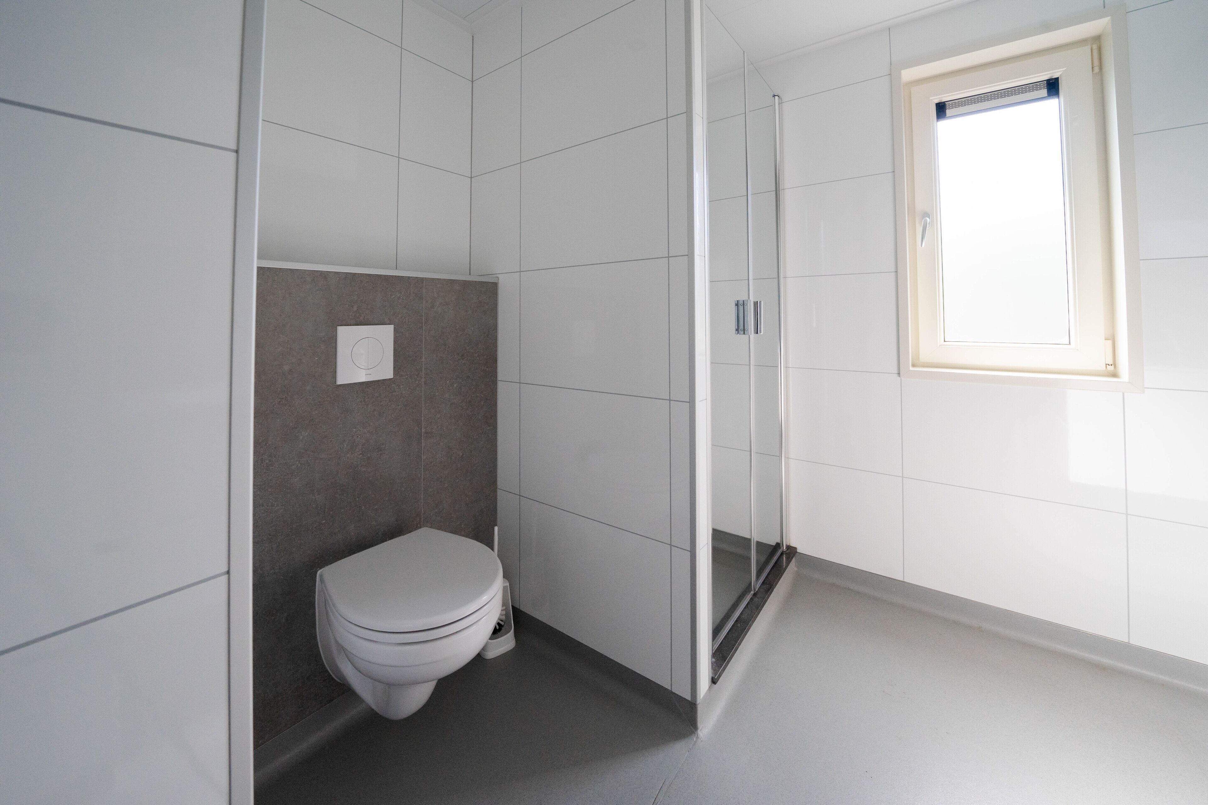 Een badkamer met toilet, douche en raam.