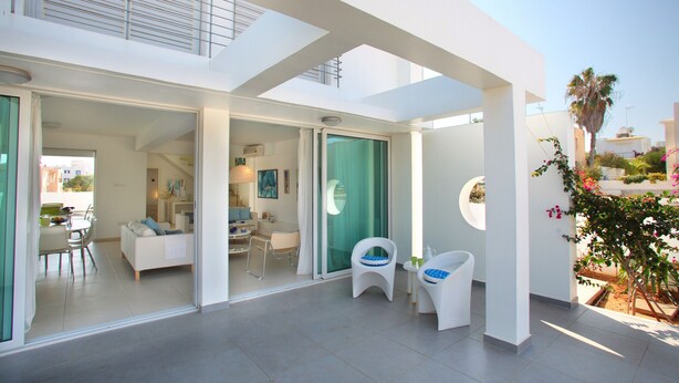 A modern interior with a dining area, a living room with a sofa and chairs, and a small seating area with two chairs. - Protaras Architects Villas (Paralimni)