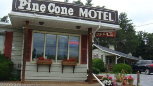 A Pine Cone Motel with a signboard, a wooden porch, and flower pots. - Pine cone Motel (Penobsquis)