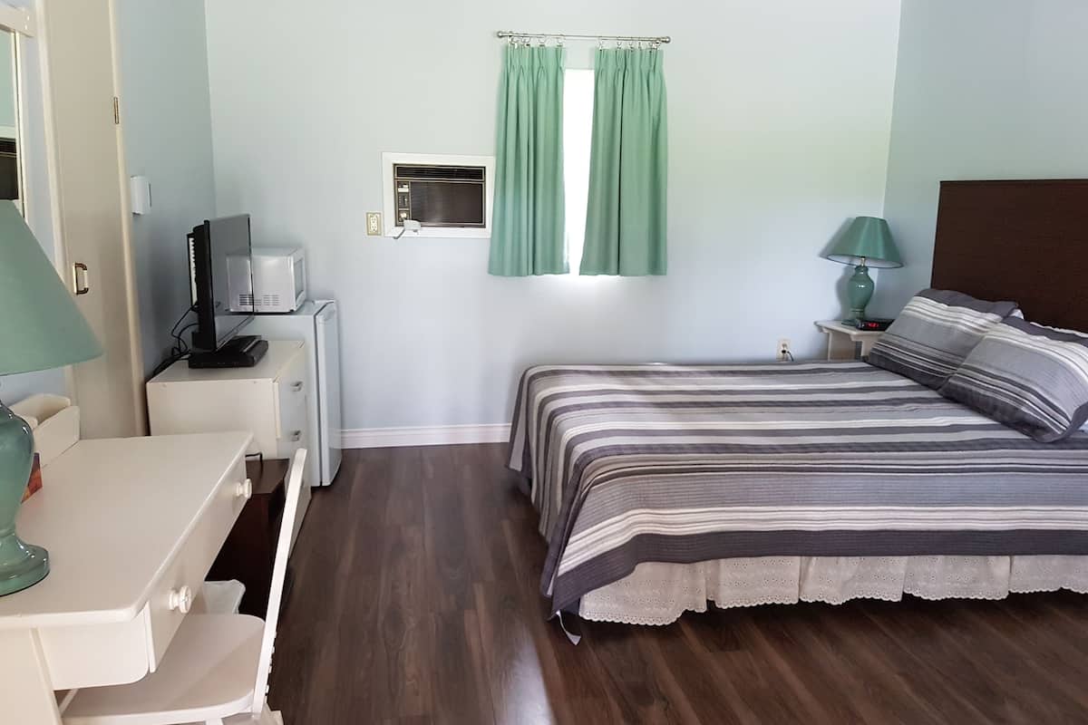 A bedroom with a bed, a desk, a television, and a window with curtains.