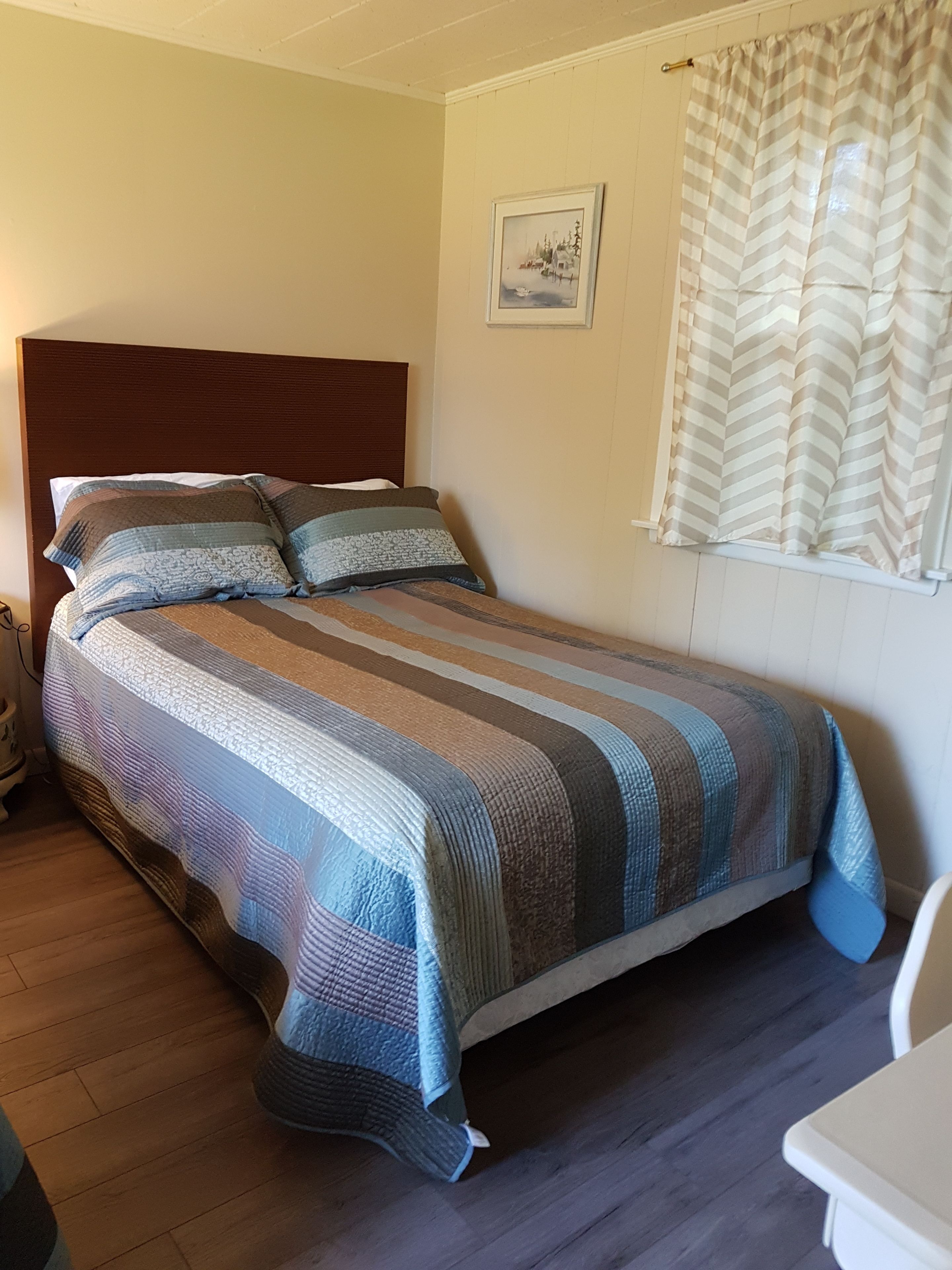 Un lit simple avec une couvre-lit à rayures, une tête de lit en bois et une fenêtre ornée de rideaux à rayures.
