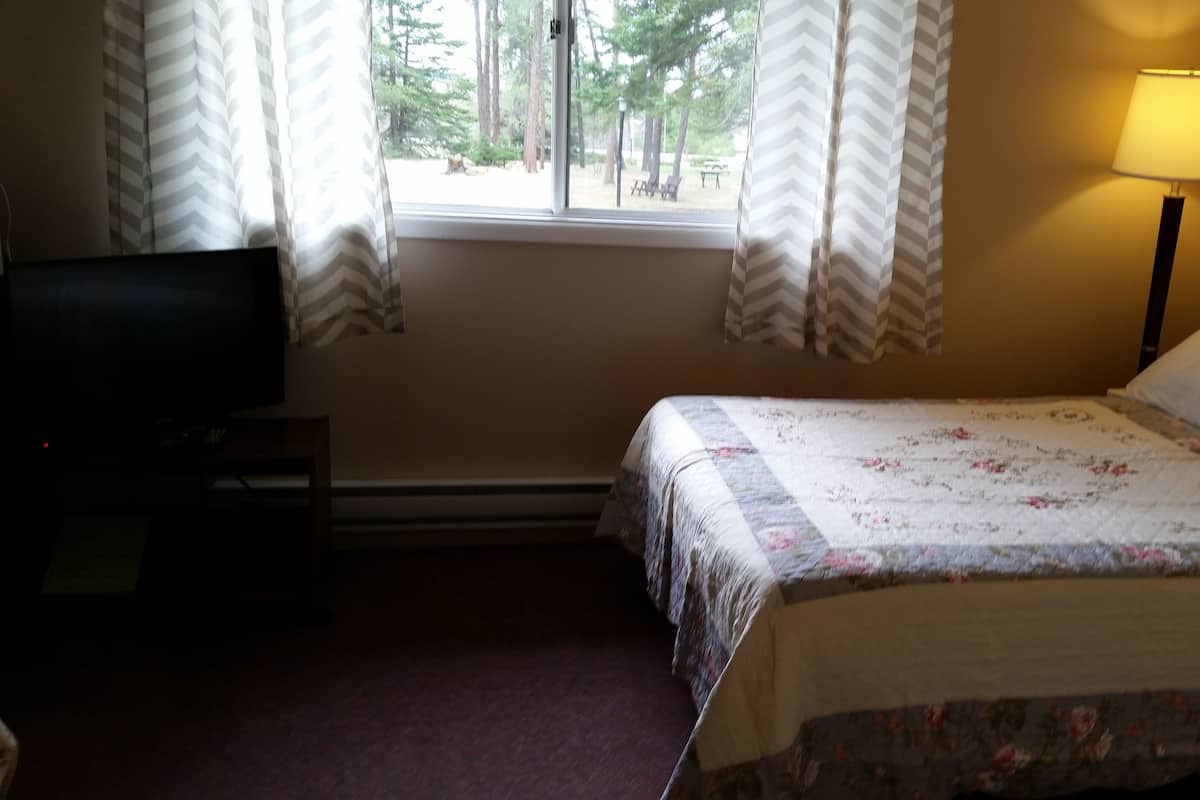 A hotel room with a bed, a TV, a lamp, and a window with curtains.