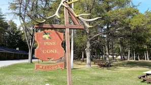 A welcome sign at Pine Cone campground with picnic tables and cabins in the background.