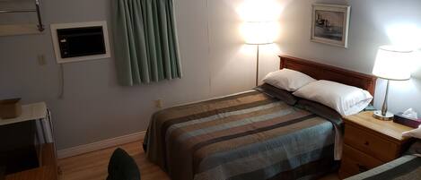 Habitación de hotel con dos camas, un escritorio con silla, un televisor de pantalla plana, una lámpara y un cuadro en la pared.
