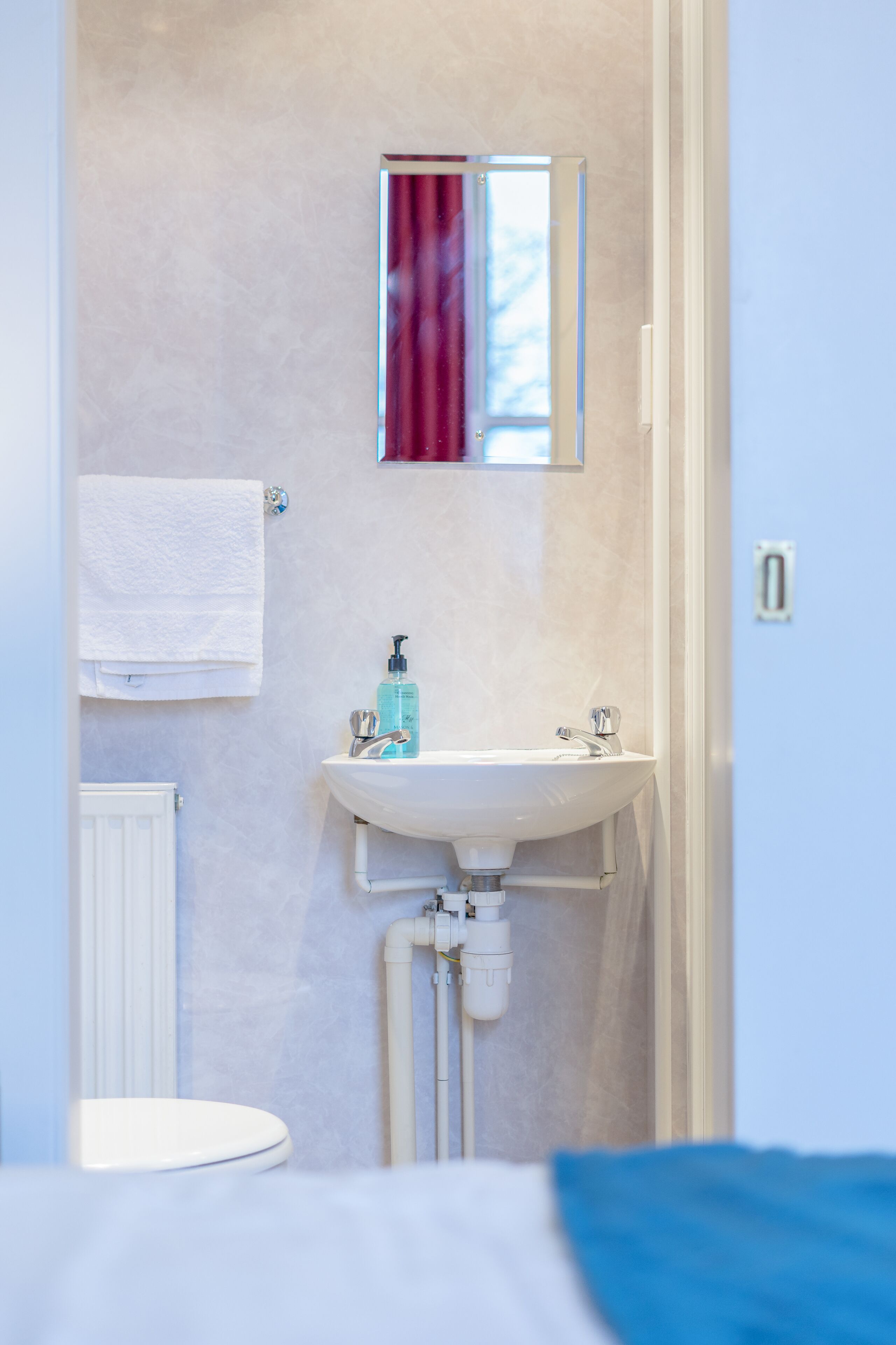 A bathroom with a white sink, a mirror, and a towel hanging on the wall.