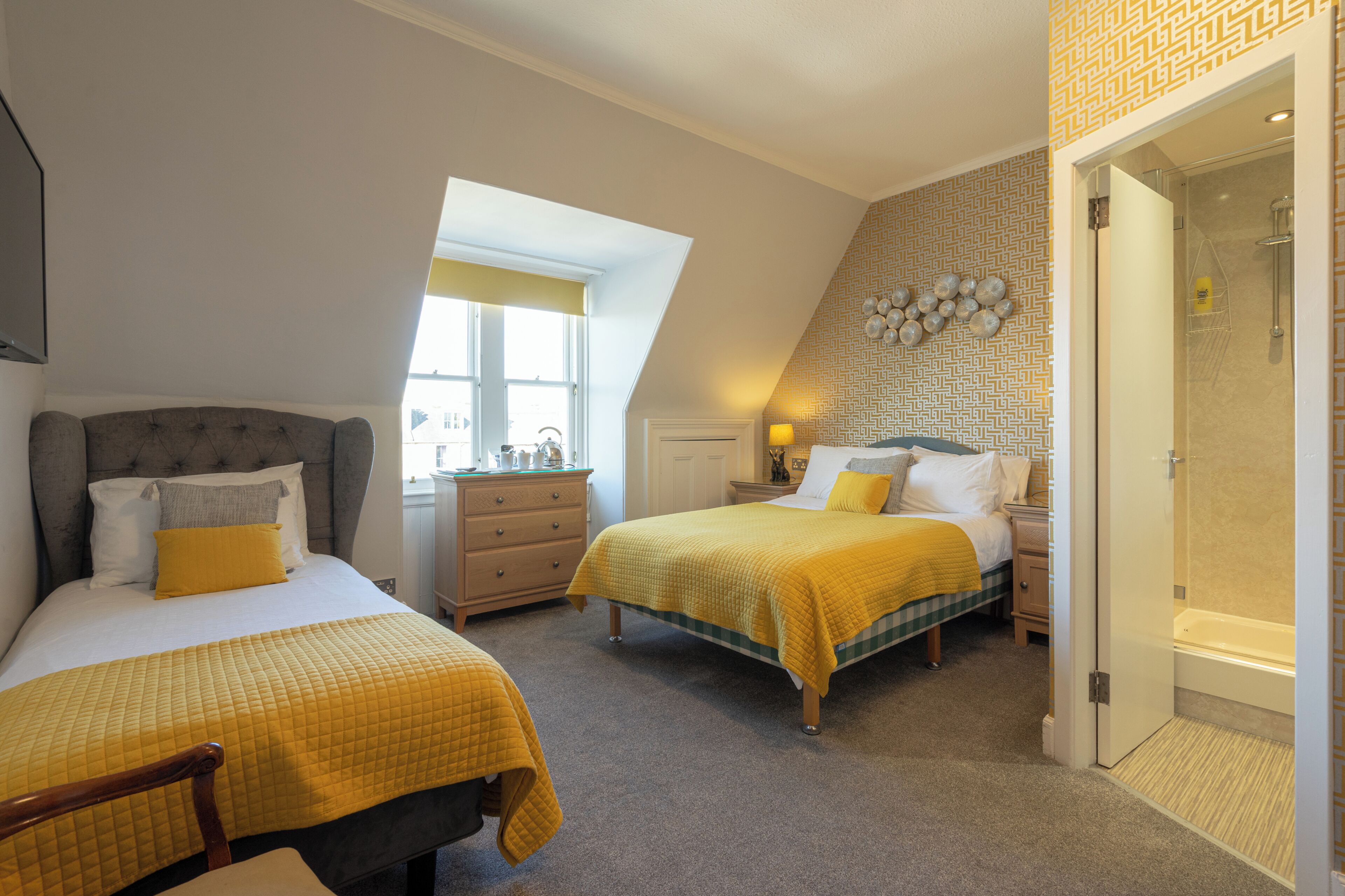 A bedroom with two beds, a dresser, a nightstand, and a bathroom with a shower.