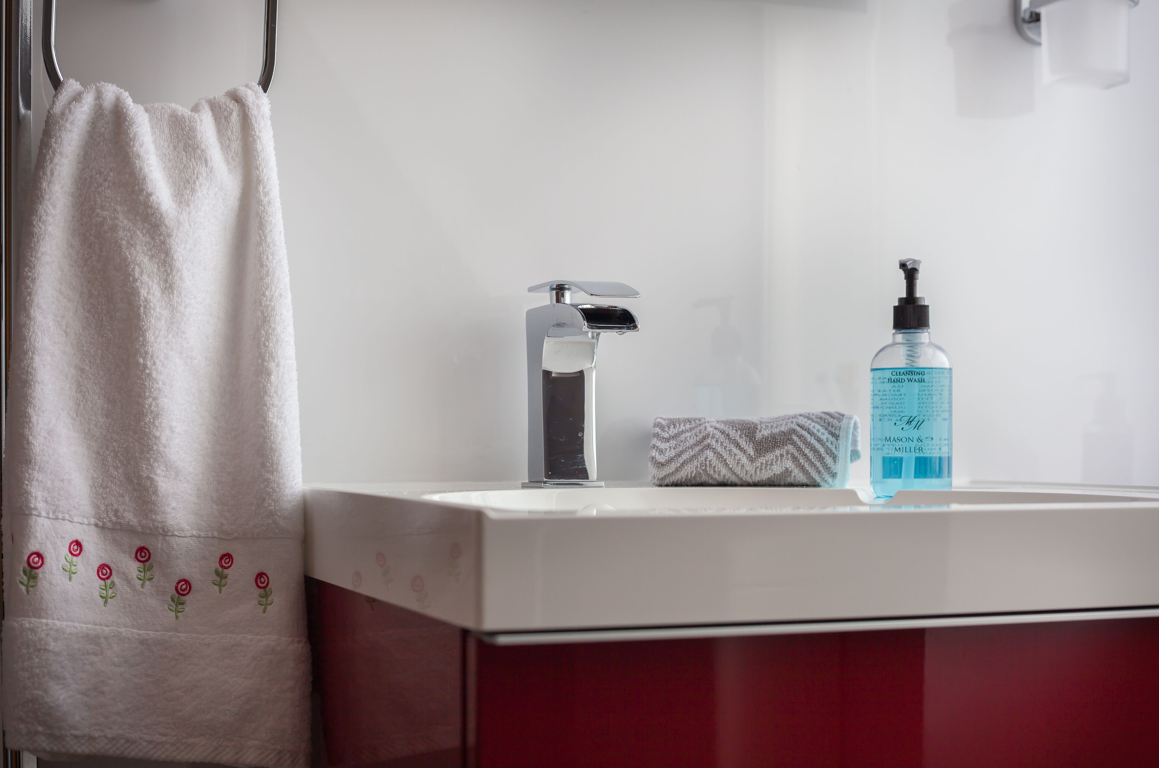 Une salle de bain avec un lavabo blanc, un robinet argenté, un flacon de savon liquide et une serviette suspendue à un porte-serviettes.