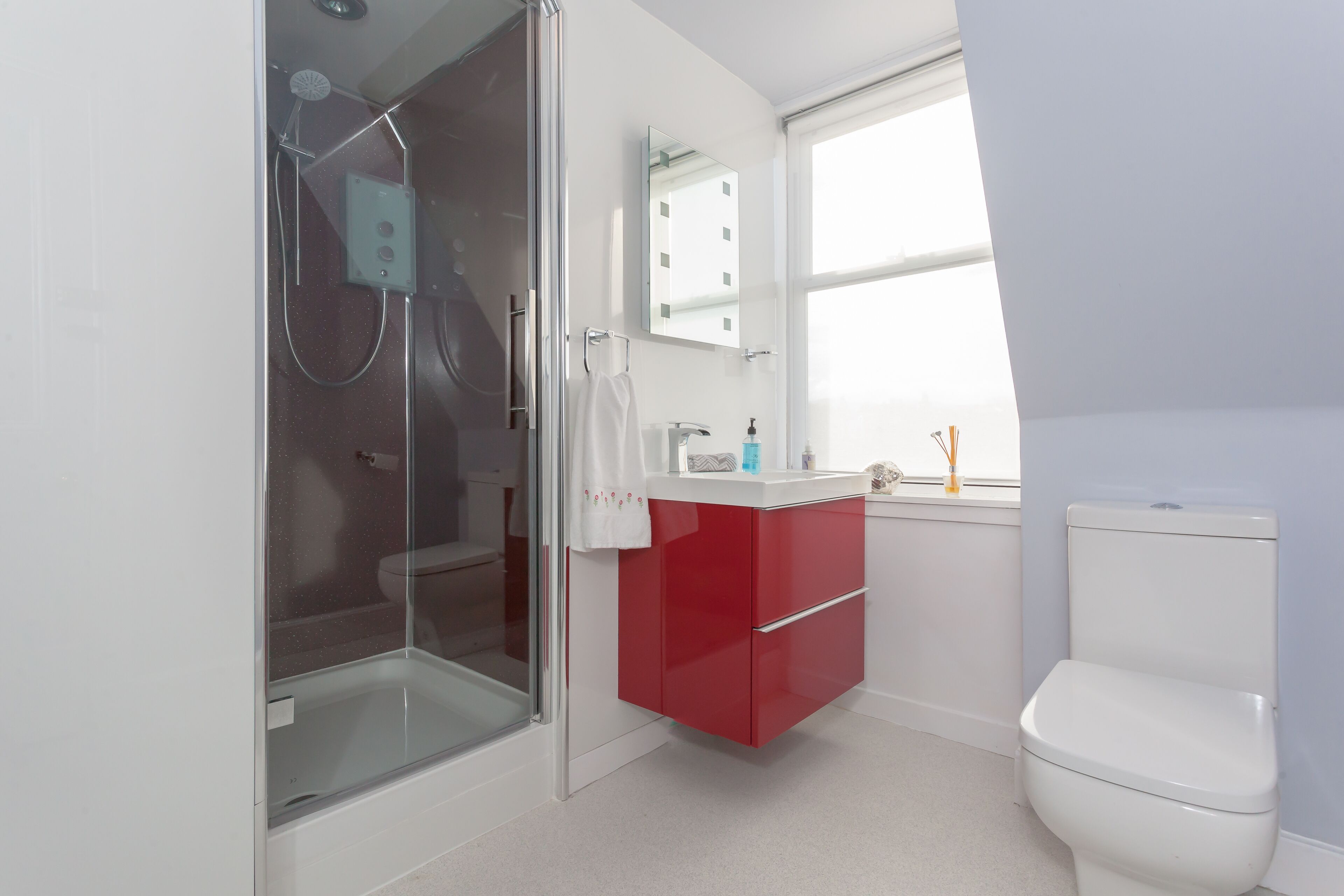 A modern bathroom with a glass-enclosed shower, a white toilet, and a red vanity with a mirror.