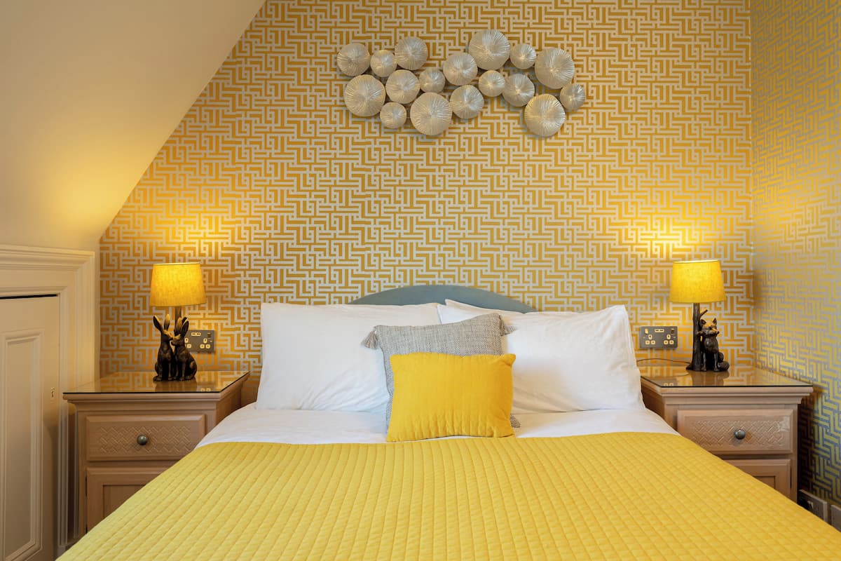 A hotel room with a bed, two bedside tables, a nightstand, a wall with a geometric pattern, and a ceiling with a circular design.
