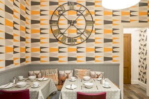 Un comedor con pared de diseño geométrico, un reloj de pared grande y una mesa preparada para cuatro.