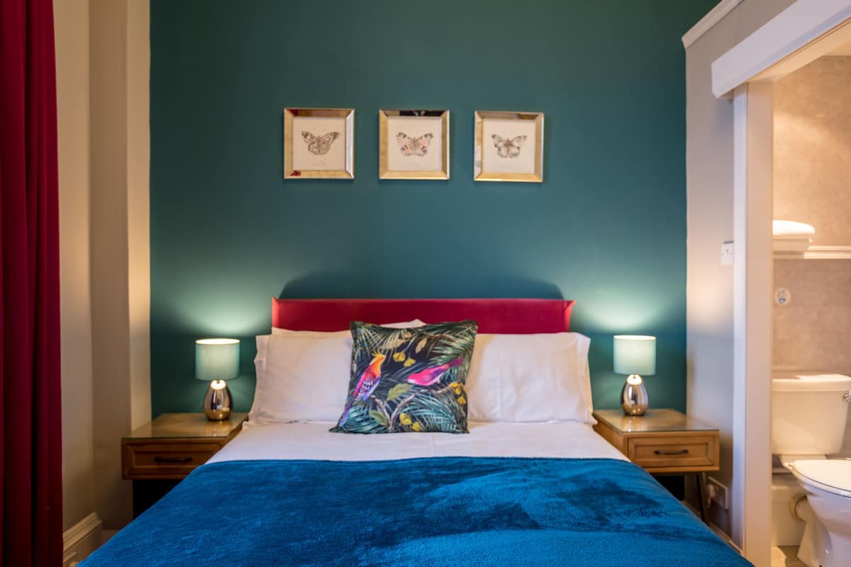 A hotel room with a bed, two bedside tables with lamps, a red headboard, and three framed butterfly pictures on the wall.