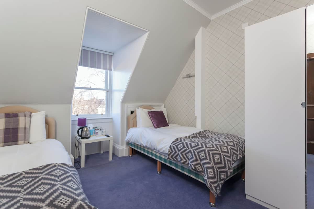 A bedroom with two beds, a small table with a kettle, and a window with a view.