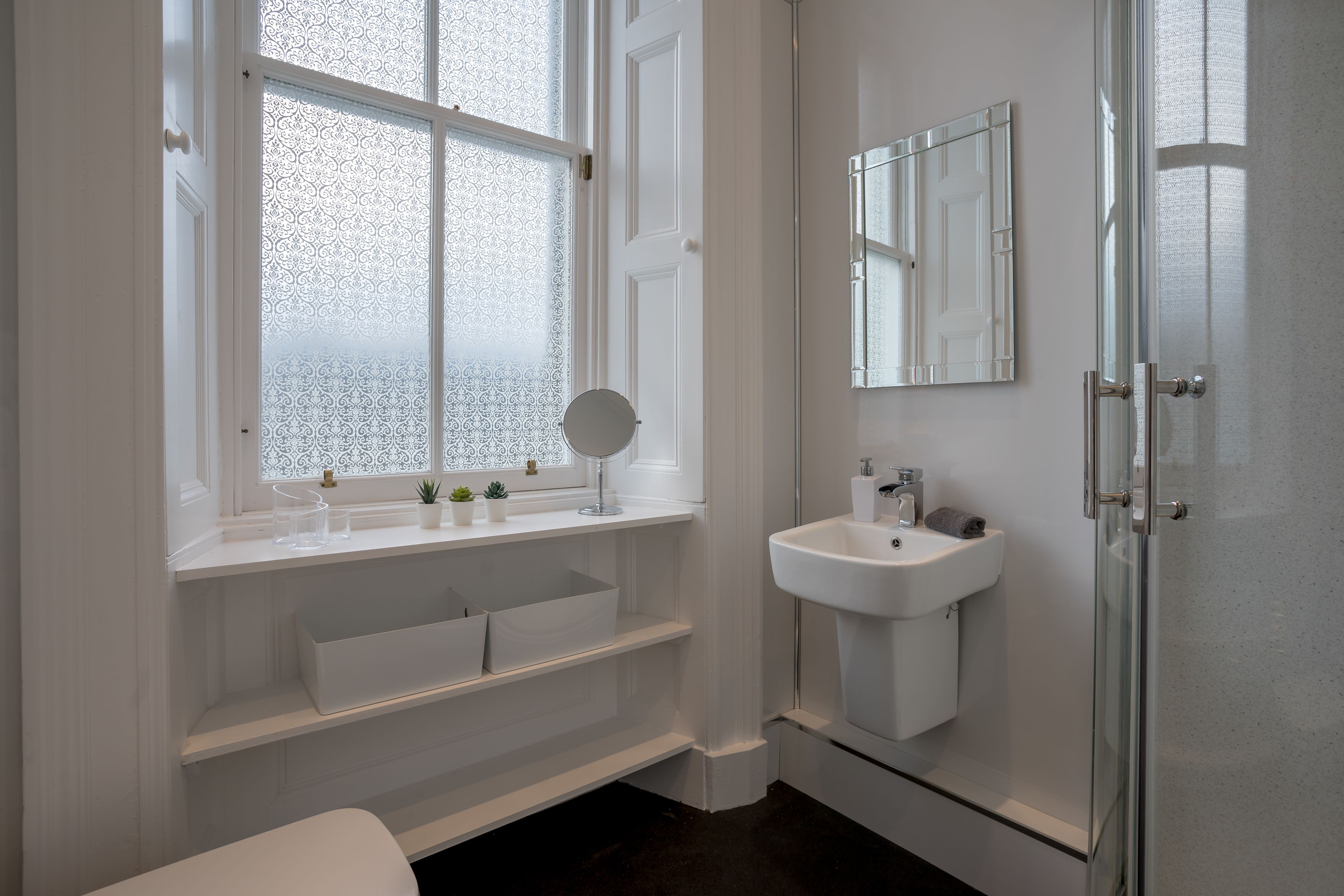 Un baño moderno con un ventanal grande, un lavamanos, un espejo y un inodoro.