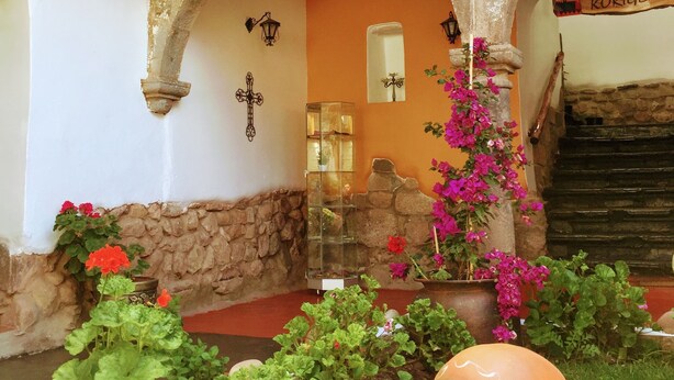 A courtyard with a stone archway, a glass display case, and a sign reading "Welcome to Korigems." - Kori Gems Inn (Cusco)