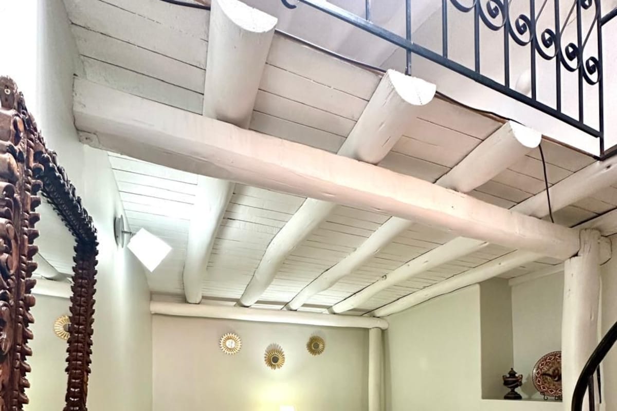 A room with two beds, a wooden floor, a ceiling with exposed beams, and a decorative mirror.