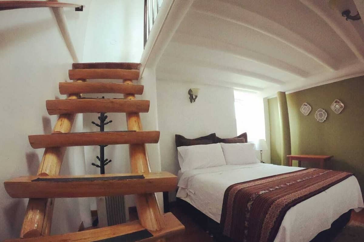 Un dormitorio con una escalera de madera, una cama con ropa blanca y una pared verde decorada con platos.
