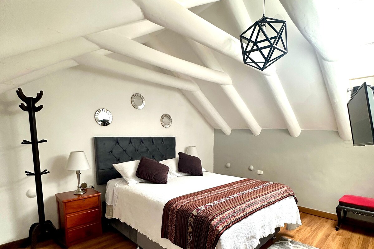 A bedroom with a bed, bedside table, lamp, coat rack, and a geometric hanging light fixture.