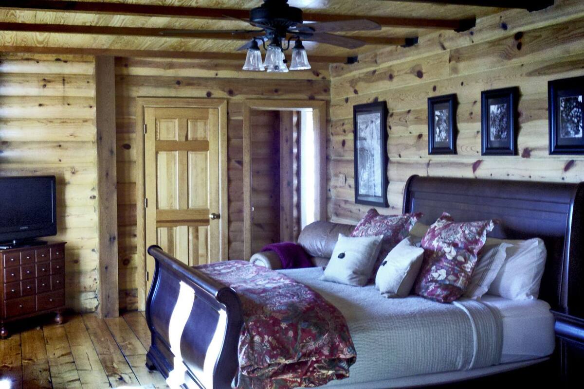 A wooden cabin bedroom with a bed, a dresser, a television, and framed pictures on the wall.